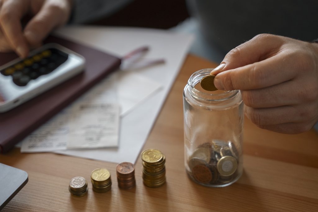 Pessoa organizando moedas e calculando saúde financeira com calculadora e boletos na mesa