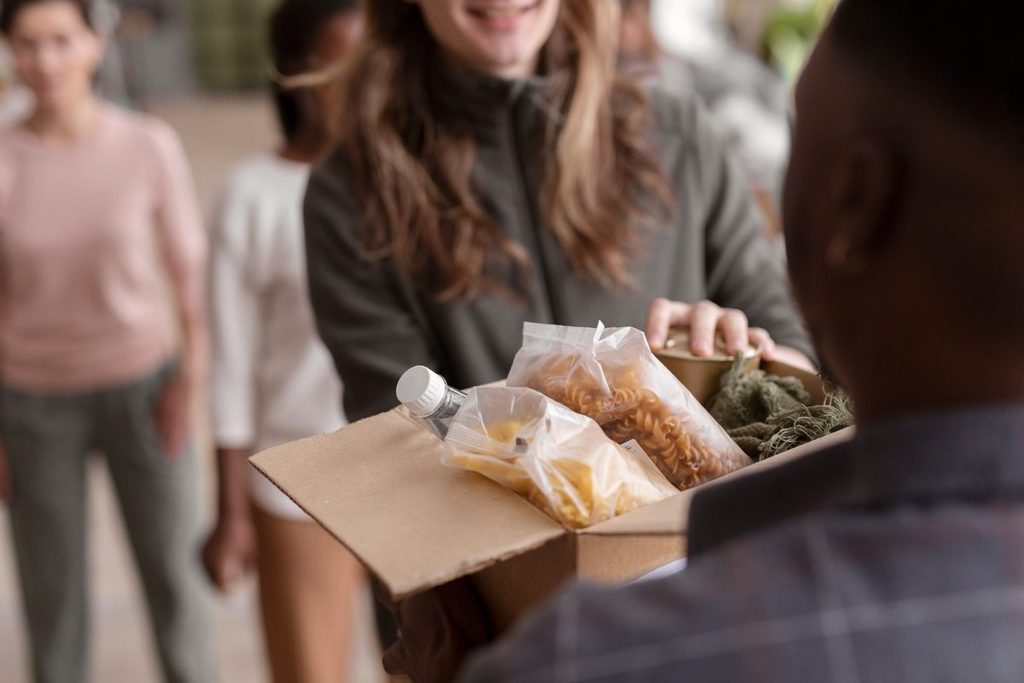 Voluntária de uma OSC entrega caixa com alimentos recebidos em doação de bens e serviços